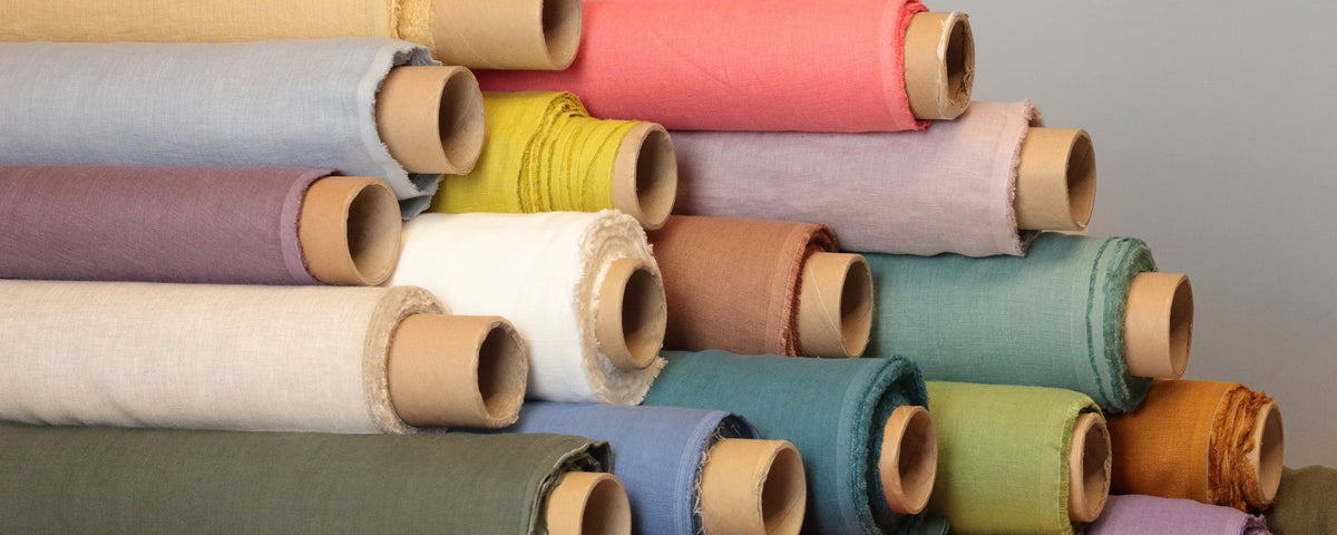 Rolls of linen fabrics of different shades of red, blue, purple, yellow, green, black and white, also different widths and densities.