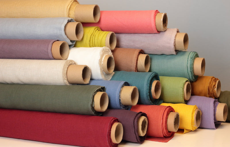 Rolls of linen fabrics of different shades of red, blue, purple, yellow, green, black and white, also different widths and densities.