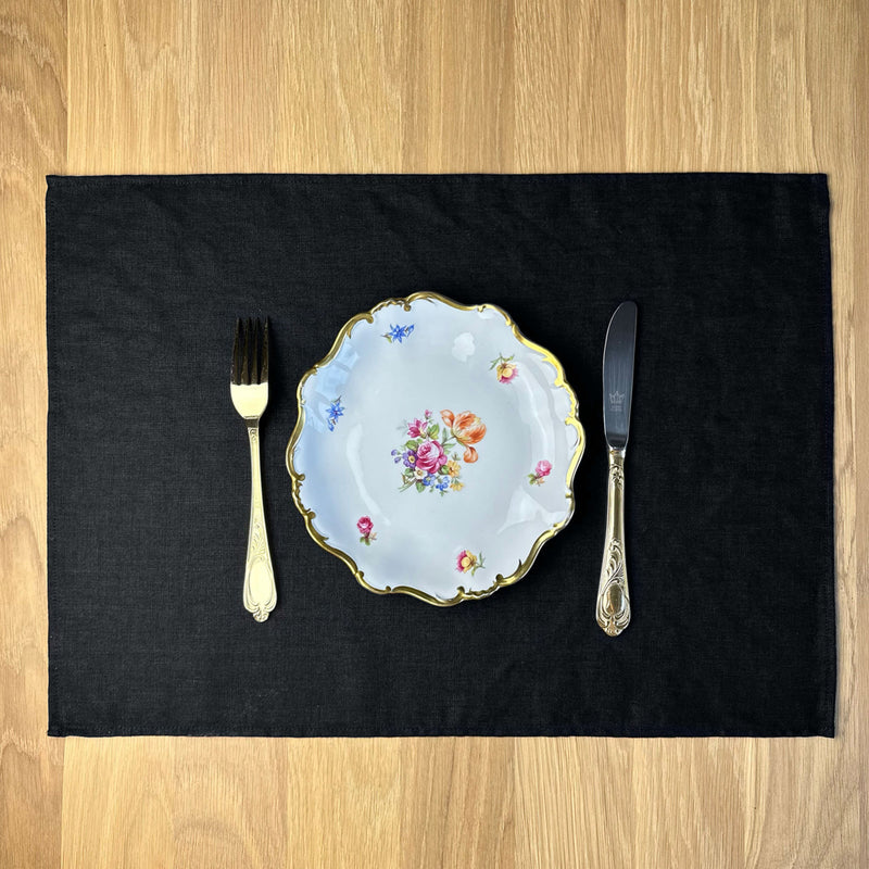 Plate-with-flowers_-fork-and-knife-on-black-linen-placemat-on-wooden-table