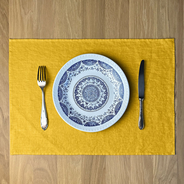 Plate-with-pattern_-fork-and-knife-on-Sunny-yellow-linen-placemat-on-wooden-table