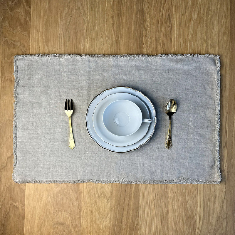 White cup fork spoon and plates on Linen placemat on wooden table