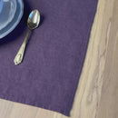 Plate-with-flowers,-knife-and-fork-on-aubergine-linen-placemat-on-wooden-table